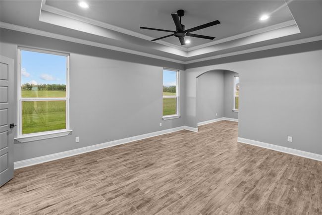 Unfurnished room with a tray ceiling, a ceiling fan, arched walkways, ornamental molding, and wood finished floors | Image 15