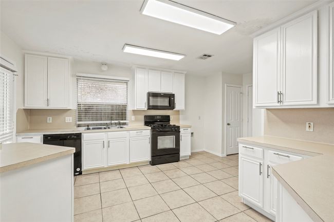 Kitchen featuring white cabinetry, black appliances, light countertops, and visible vents | Image 8
