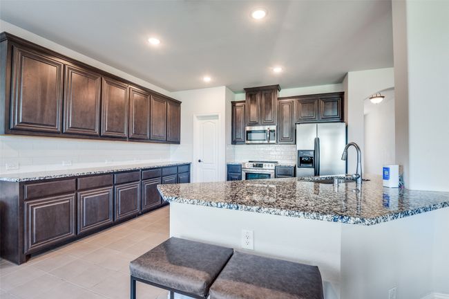 Kitchen with stainless steel appliances, dark stone countertops, dark brown cabinets, light tile patterned floors, and a peninsula | Image 8