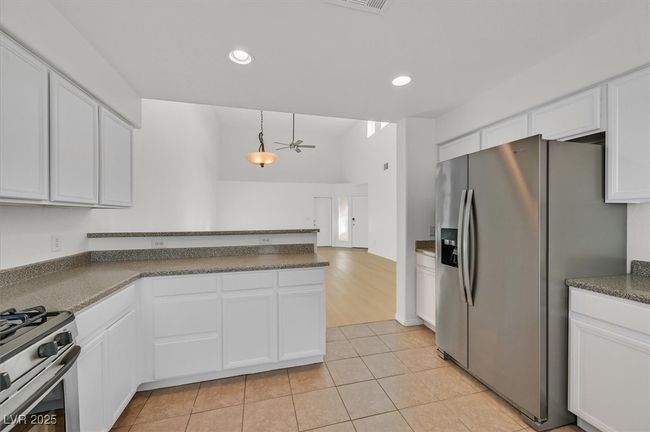 Kitchen with stainless steel appliances, a peninsula, white cabinets, dark countertops, and light tile patterned flooring | Image 7