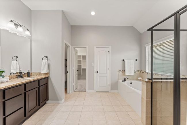 The spa like primary bath offers dual sinks, granite countertops, a walk-in shower with decorative tile accents, a relaxing soaking tub and direct access to the spacious walk-in closet | Image 26
