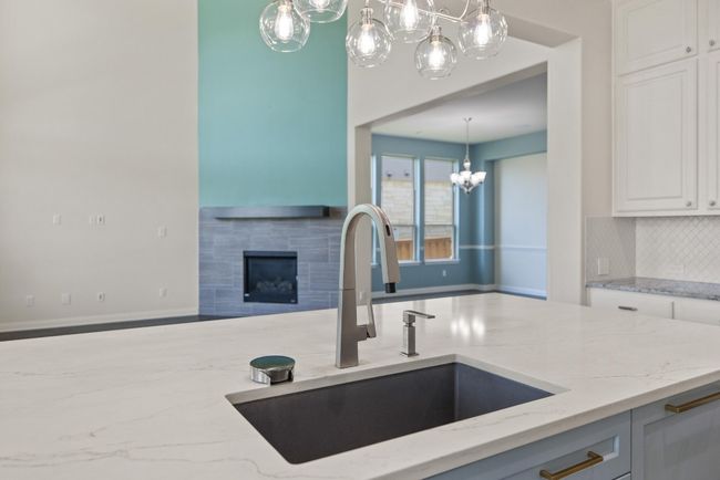 Kitchen featuring a chandelier, light stone countertops, backsplash, a tiled fireplace, and white cabinets | Image 7
