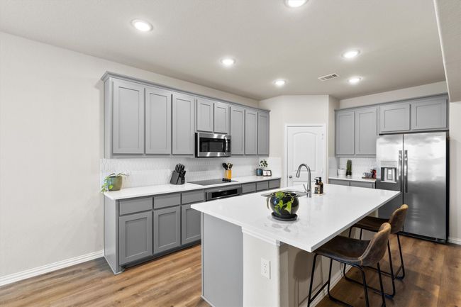 Kitchen with gray cabinets, stainless steel appliances, backsplash, an island with sink, and a kitchen breakfast bar | Image 10