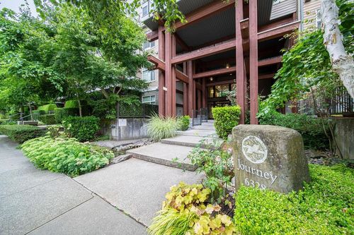 Building entrance featuring a wood-beam portico, concrete steps, and integrated landscaping with diverse plantings | Card Image