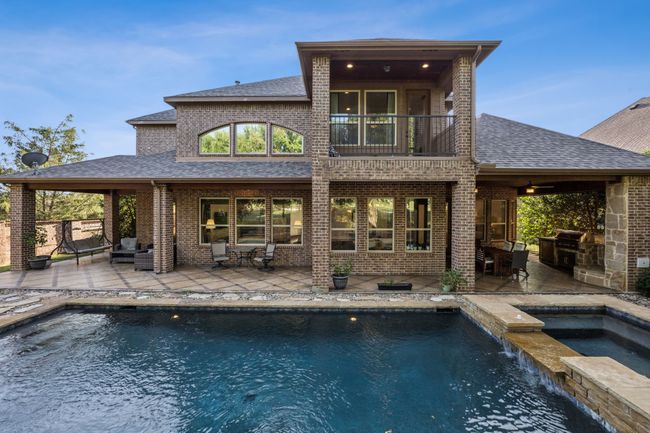 Rear view of house featuring a balcony, an in-ground hot tub, a shingled roof, brick siding, and a patio area | Image 30