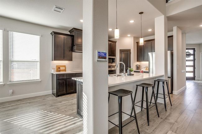 Kitchen featuring light wood-type flooring, dark brown cabinetry, stainless steel appliances, sink, and decorative light fixtures | Image 4