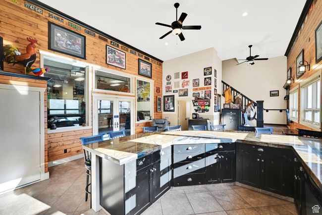 Kitchen featuring ceiling fan, light tile patterned flooring, wooden walls, and a breakfast bar | Image 39