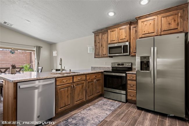 Kitchen with appliances with stainless steel finishes, a sink, a peninsula, vaulted ceiling, and brown cabinets | Image 31