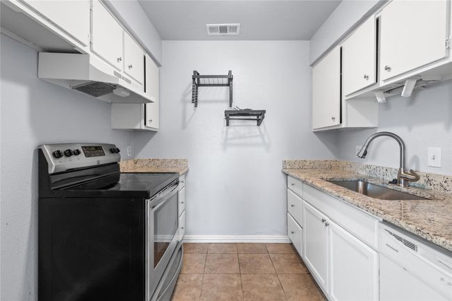 Kitchen featuring stainless steel electric range oven, white dishwasher, white cabinets, light tile patterned floors, and light stone counters | Image 12