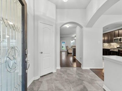 This is a modern and spacious entryway that leads directly into an open-plan living space, featuring elegant archways, hardwood floors, and a contemporary kitchen with dark cabinetry and stainless steel appliances. | Image 3