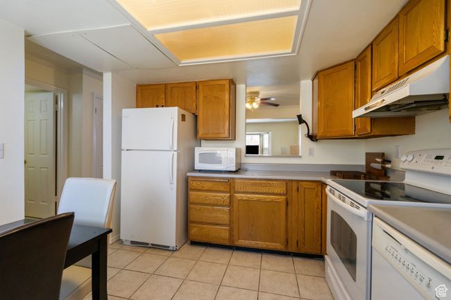 Kitchen featuring brown cabinets, white appliances, and under cabinet range hood | Image 7