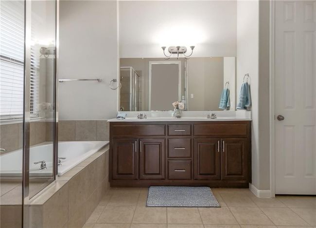 Full bath featuring tile patterned flooring, double vanity, a garden tub, a stall shower, and a chandelier | Image 17