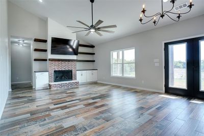 Unfurnished living room with ceiling fan with notable chandelier, a fireplace, french doors, high vaulted ceiling, and hardwood / wood-style flooring | Image 3