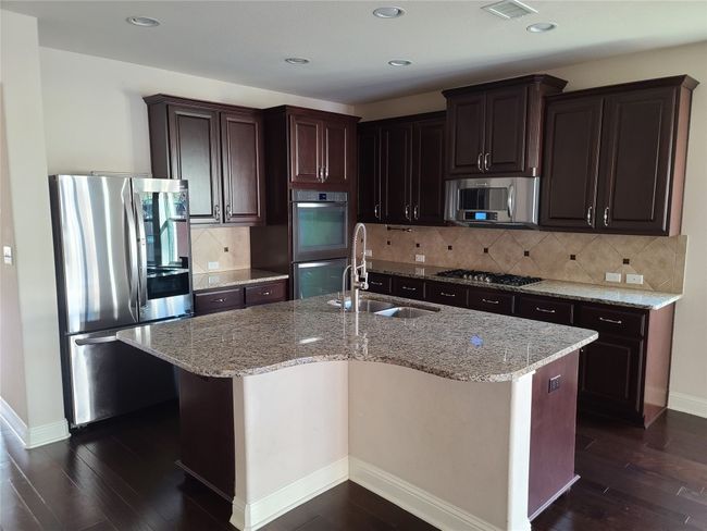 Kitchen with appliances with stainless steel finishes, dark wood-style floors, a kitchen island with sink, light stone countertops, and recessed lighting | Image 9