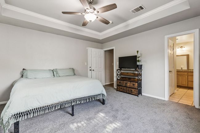 Bedroom featuring ornamental molding, carpet, a raised ceiling, ensuite bath, and ceiling fan | Image 16