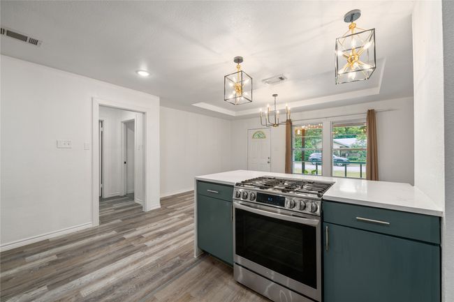 Kitchen with stainless steel range with gas cooktop, a tray ceiling, a chandelier, wood finished floors, and light countertops | Image 8