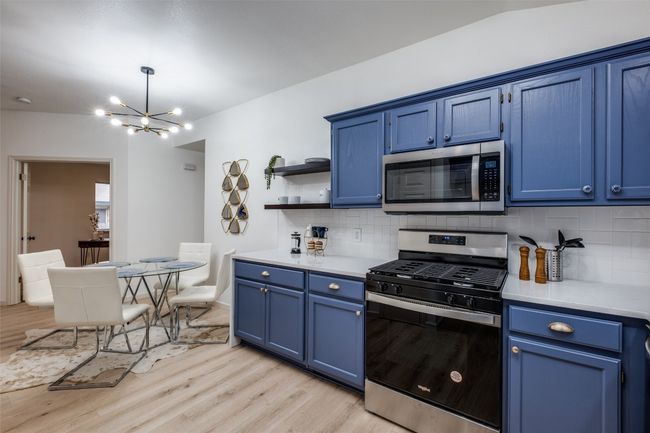 Kitchen featuring a notable chandelier, light countertops, blue cabinets, and appliances with stainless steel finishes | Image 12
