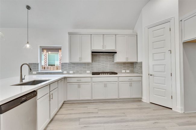 Kitchen with stainless steel dishwasher, light countertops, decorative backsplash, cooktop, and vaulted ceiling | Image 5