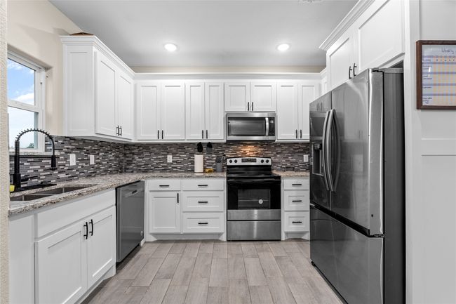 Kitchen featuring appliances with stainless steel finishes, white cabinetry, light wood-type flooring, backsplash, and recessed lighting | Image 23