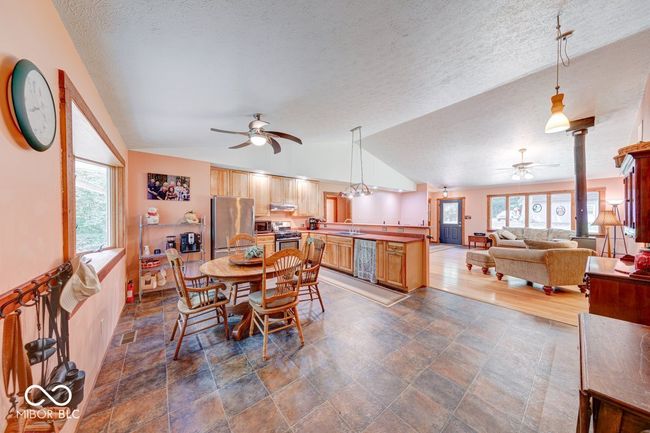 dining room featuring a ceiling fan, vaulted ceiling, plenty of natural light, a textured ceiling, and dark stone finish floors | Image 46