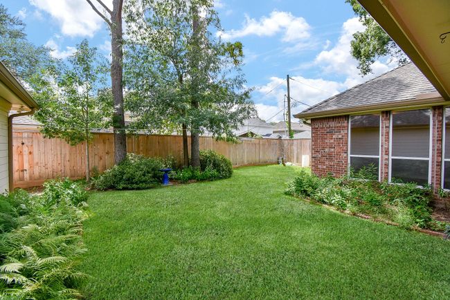 This photo showcases a well-maintained backyard featuring lush green grass, mature trees, and a tidy garden bed. It has a wooden privacy fence and the side of a brick house with large windows. Ideal for outdoor relaxation and privacy. | Image 47