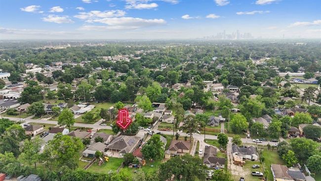 This aerial photo highlights a residential neighborhood with an array of single-family homes, lush greenery, and mature trees. The property for sale is clearly marked with a red arrow. In the distance, the city skyline suggests close proximity to urban amenities and conveniences. | Image 11