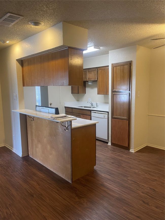 Kitchen featuring dishwasher, dark wood-style flooring, light countertops, a textured ceiling, and a peninsula | Image 6