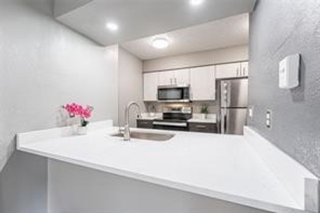 Kitchen featuring stainless steel appliances, a peninsula, light countertops, white cabinetry, and a textured wall | Image 11
