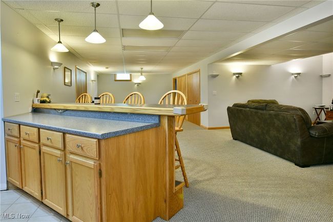 Kitchen featuring a kitchen breakfast bar, light colored carpet, decorative light fixtures, open floor plan, and a drop ceiling | Image 41