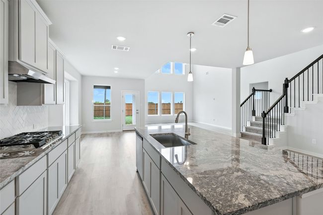 Kitchen with appliances with stainless steel finishes, open floor plan, under cabinet range hood, tasteful backsplash, and pendant lighting | Image 6