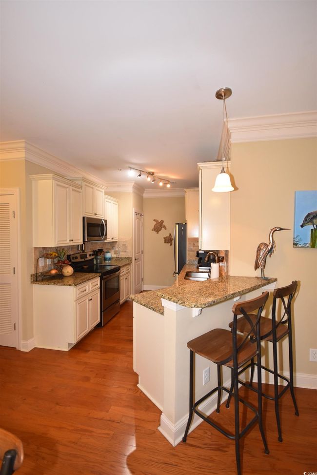 Kitchen featuring stainless steel appliances, crown molding, a kitchen bar, backsplash, and a peninsula | Image 10