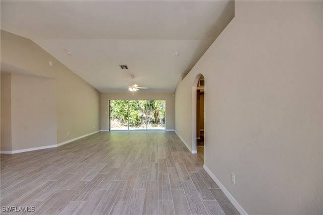 Empty room featuring arched walkways, light wood-type flooring, lofted ceiling, and visible vents | Image 9