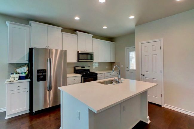 Kitchen featuring decorative backsplash, stainless steel appliances, an island with sink, a sink, and dark wood-style floors | Image 8