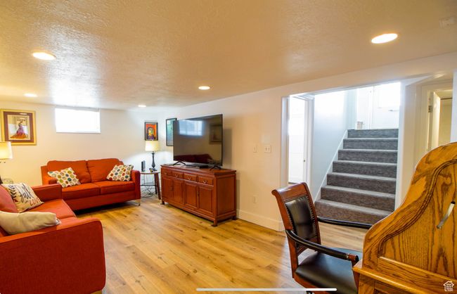Living area with light wood finished floors, stairs, a textured ceiling, recessed lighting, and baseboards | Image 18