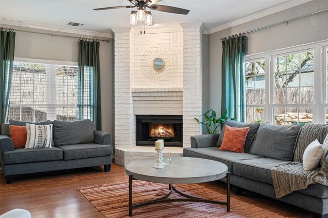 Living room with a brick fireplace, crown molding, visible vents, a ceiling fan, and wood finished floors | Image 21