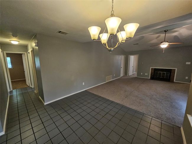 Unfurnished living room with dark tile patterned floors, visible vents, a fireplace, and dark colored carpet | Image 12