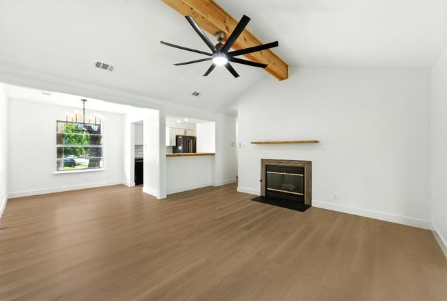 Unfurnished living room with a fireplace with flush hearth, wood finished floors, a chandelier, and a ceiling fan | Image 5