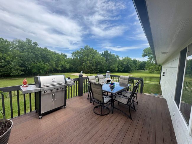 Wooden terrace featuring outdoor dining space, a lawn, area for grilling, and view of scattered trees | Image 27