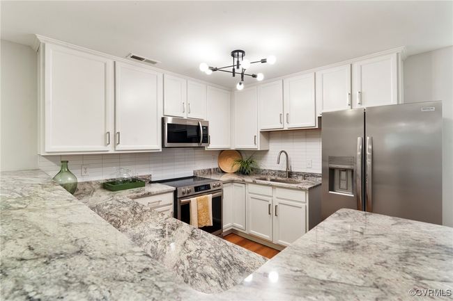 Kitchen with appliances with stainless steel finishes, white cabinetry, decorative backsplash, light stone counters, and light wood-type flooring | Image 6