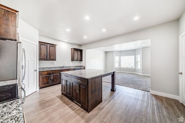 Kitchen with dark brown cabinetry, recessed lighting, a center island, light stone countertops, and light wood finished floors | Image 9
