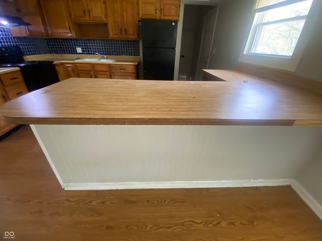 kitchen with light countertops, black appliances, a sink, baseboards, and a peninsula | Image 6