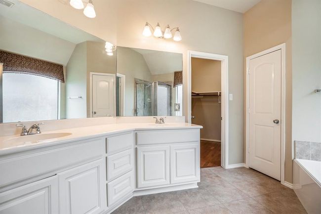 The spacious primary bathroom features a clean, airy design with dual vanities, a large wall mirror, and plenty of storage. The separate soaking tub and walk-in shower offer the perfect space to unwind, while the neutral tones and natural light create a calming spa-like atmosphere. | Image 20
