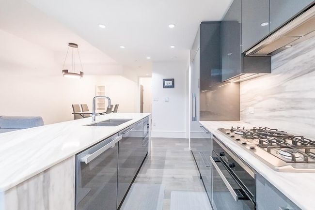Kitchen with under cabinet range hood, stainless steel appliances, a sink, modern cabinets, and decorative light fixtures | Image 10