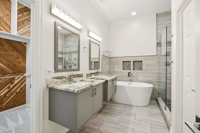 Bathroom featuring a shower stall, a freestanding bath, double vanity, ornamental molding, and tile walls | Image 18