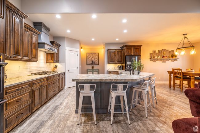 Kitchen featuring stainless steel appliances, ventilation hood, light countertops, a kitchen breakfast bar, and backsplash | Image 14