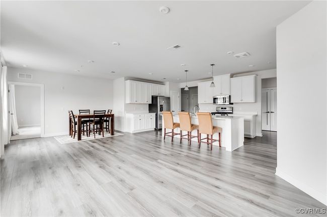 Kitchen featuring stainless steel appliances, light countertops, a kitchen island with sink, white cabinetry, and light wood finished floors | Image 9