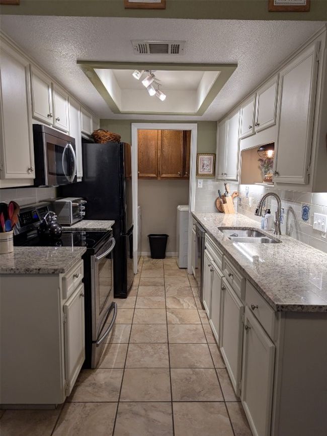 Kitchen featuring appliances with stainless steel finishes, washer and dryer, tasteful backsplash, a tray ceiling, and a textured ceiling | Image 12