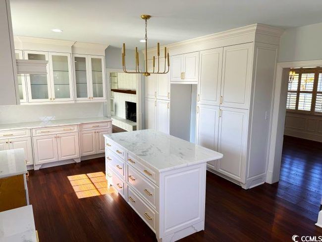 Kitchen featuring white cabinetry, light stone countertops, hanging light fixtures, a chandelier, and dark wood-type flooring | Image 7