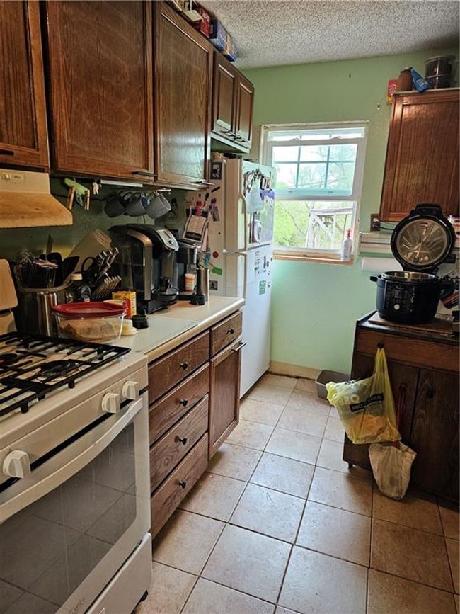 Kitchen featuring a textured ceiling, range, light countertops, exhaust hood, and refrigerator | Image 13
