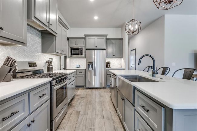 Kitchen with a sink, stainless steel appliances, light countertops, a notable chandelier, and gray cabinetry | Image 36